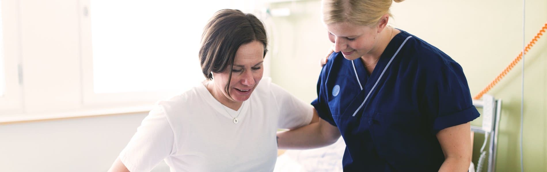 Vårdpersonal hjälper sittande patient resa sig upp