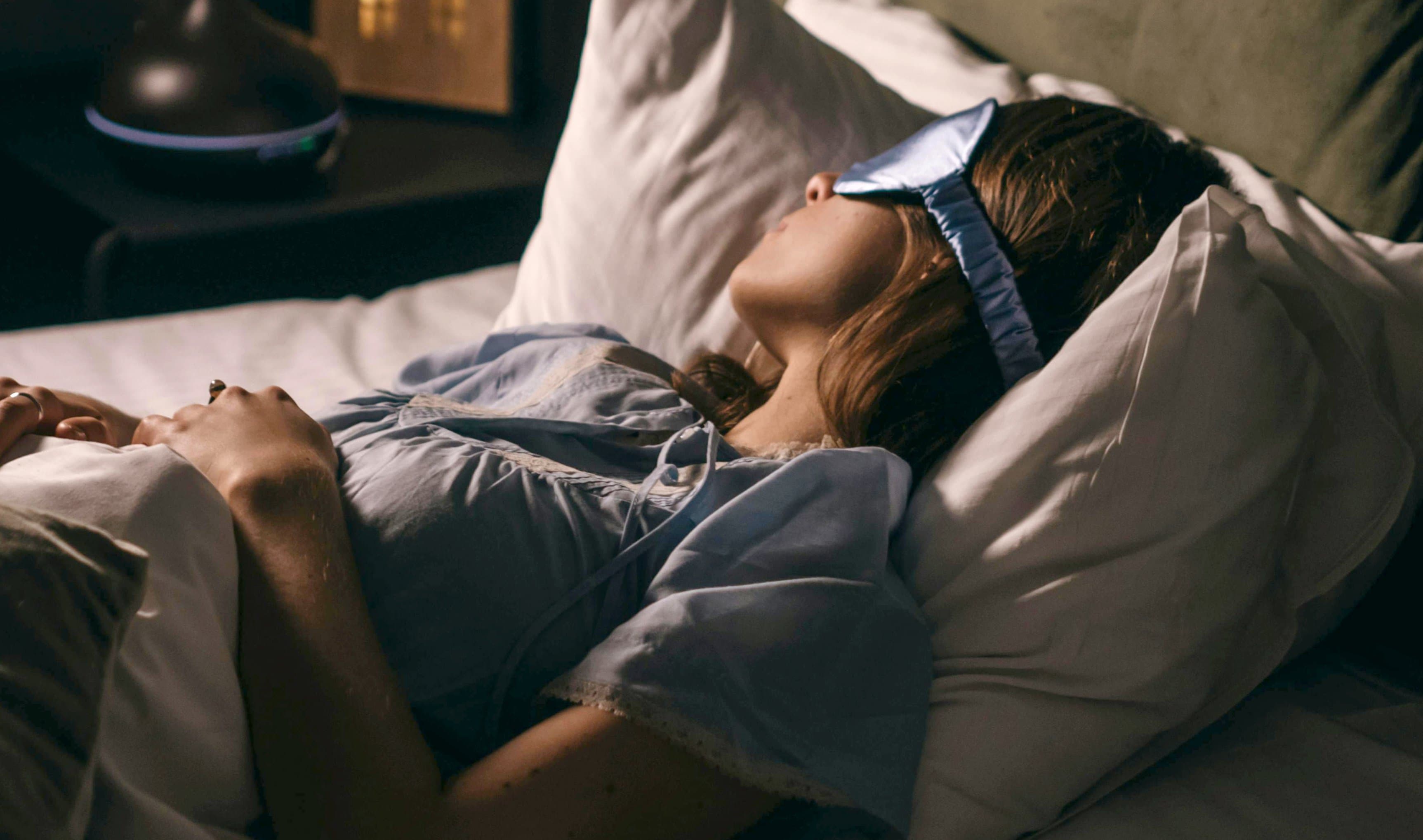 Person som ligger i sängen sovandes med ögonmask Person som ligger i sängen sovandes med ögonmask